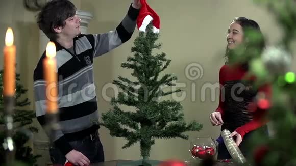 年轻人和女人在圣诞树上挂圣诞老人的帽子视频的预览图