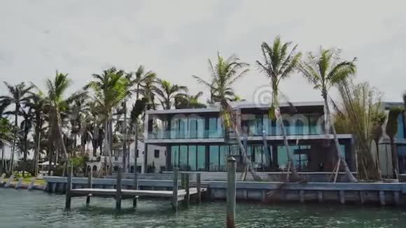 迈阿密阳光明媚的艾尔斯海滩海湾沿岸棕榈树之间的豪华大房子视频的预览图