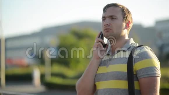 年轻人拿着手机用智能手机打电话打电话站在阳光明媚的街道上视频的预览图