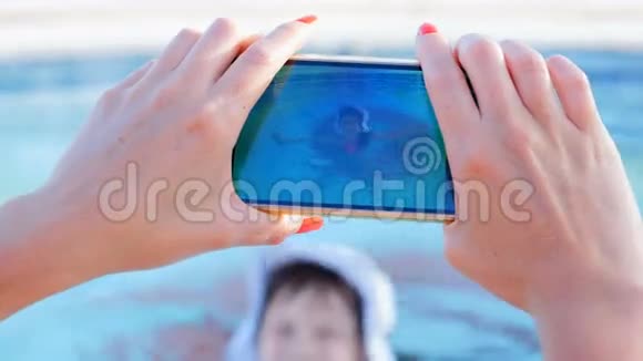 美丽的女孩在游泳池里的一个小女孩在设备上拍摄视频视频的预览图