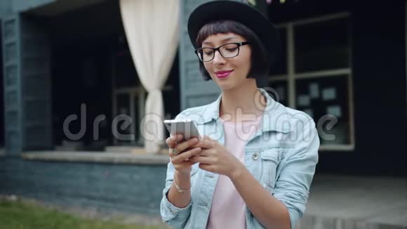 快乐的女孩在户外使用智能手机微笑着触摸屏幕享受设备视频的预览图