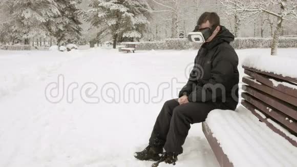 一个冬天在雪地公园里戴着虚拟现实耳机的人他试图触摸虚拟物体一个穿着视频的预览图