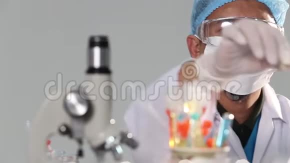 亚洲男子医生带口罩橡胶头盔和眼罩检查液体化学物质滴入玻璃管板红色蓝色视频的预览图