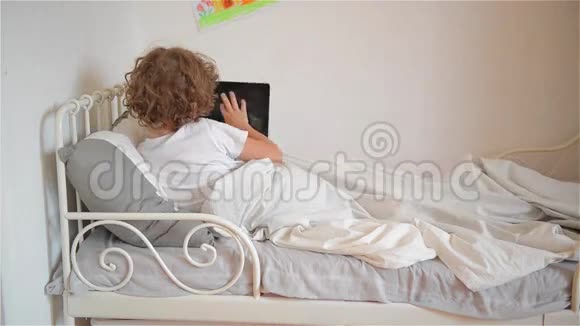 可爱的小男孩在床上玩数字平板电脑游戏视频的预览图