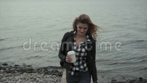 漂亮的金发女郎手里拿着一杯咖啡靠近大海视频的预览图