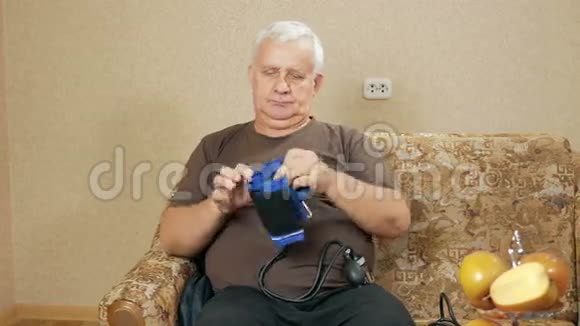 超重老人在沙发上测量自己家的压力他通过血压计听脉搏视频的预览图