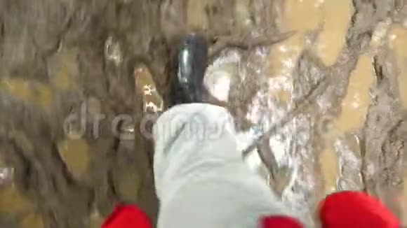 人在泥泞的水坑里踏着橡胶靴的顶部景色双腿在泥坑里鞋上满是洞视频的预览图