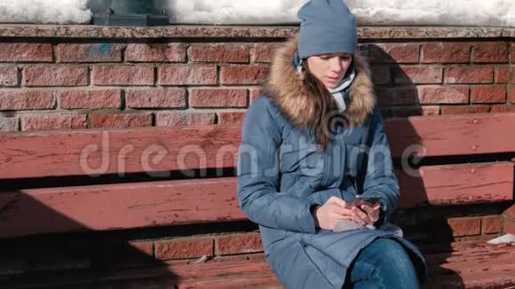 女人坐在冬季公园的手机上浏览网页视频的预览图