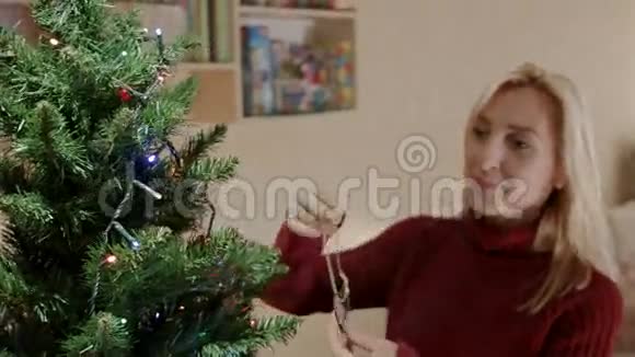 穿红色套头衫的金发女人用圣诞鹿来装饰圣诞树视频的预览图