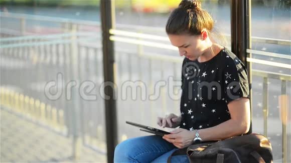 年轻女子在火车站等公共交通工具时看着她的平板电脑或电子书视频的预览图