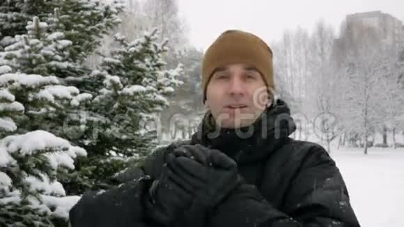 一个年轻人看着相机在冬天的森林里玩雪它做雪球并投掷它们冬季视频的预览图