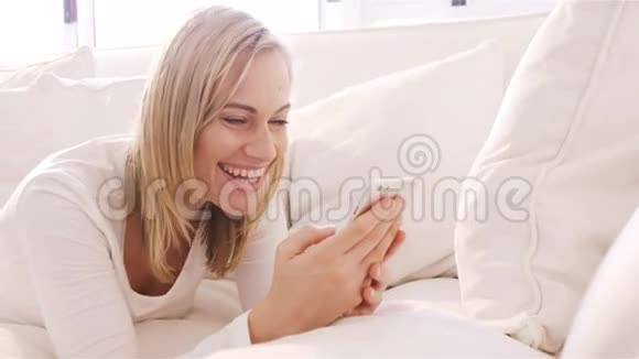金发女人用智能手机躺在沙发上微笑着视频的预览图