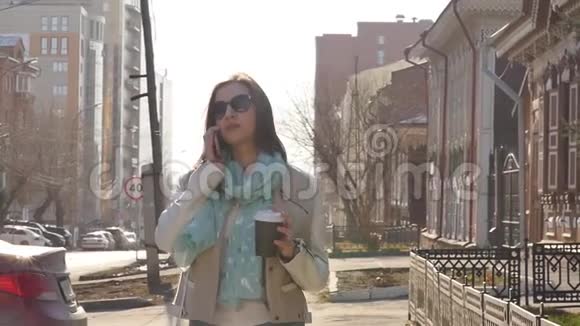 年轻的商务女性在街上散步午餐休息时喝咖啡使用智能手机视频的预览图