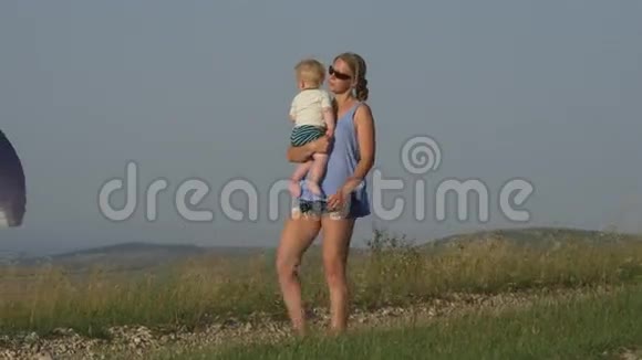 妈妈带着婴儿在滑翔伞的背景下行走视频的预览图