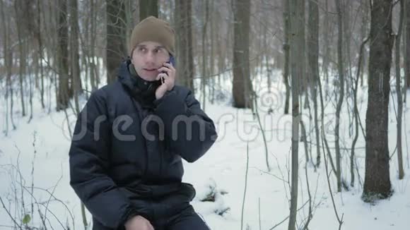 年轻人坐在冬林里打电话他钦佩雪和树的两边一个黑暗中的人视频的预览图