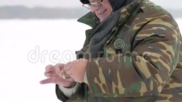 那个人在冰上钓鱼钓到一条小鱼他把它从钩子上拿下来扔到冰上穿着防护衣视频的预览图