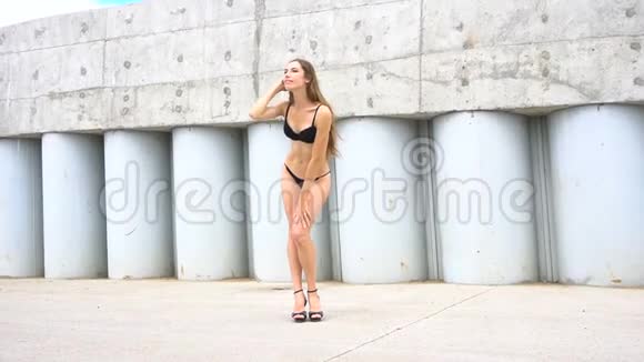 穿比基尼的年轻女子在水泥墙的背景上摆姿势视频的预览图