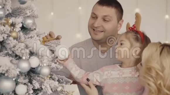 爸爸妈妈和小女孩幸福的年轻家庭装饰圣诞树视频的预览图