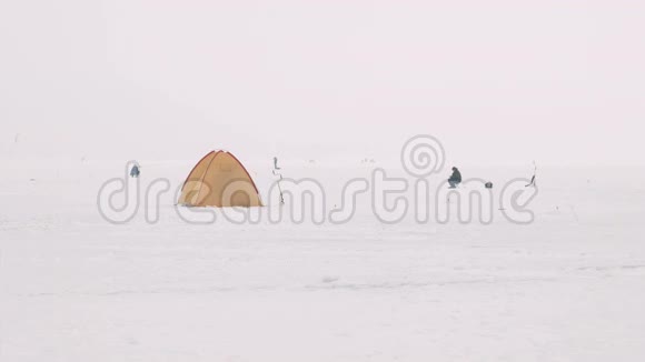 在冰冻的湖面上的看台上放着过冬的帐篷坐在附近的几个渔民视频的预览图