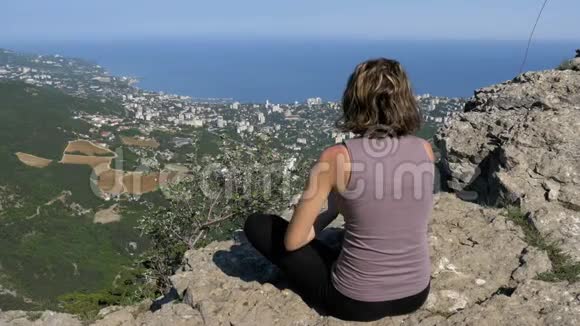 坐在莲花位置的女人练习瑜伽动作或冥想并在山上举起她的手臂视频的预览图