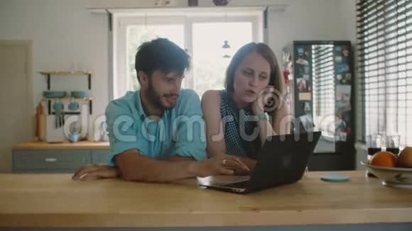 年轻漂亮的夫妇正坐在厨房的桌子旁看着电脑说话慢动作视频的预览图