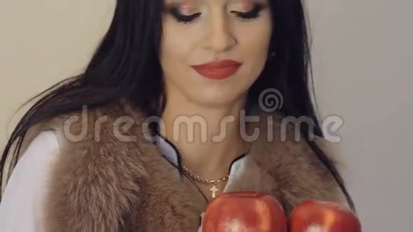 热情的女孩穿着毛茸茸的夹克摆着两个红苹果慢慢地视频的预览图