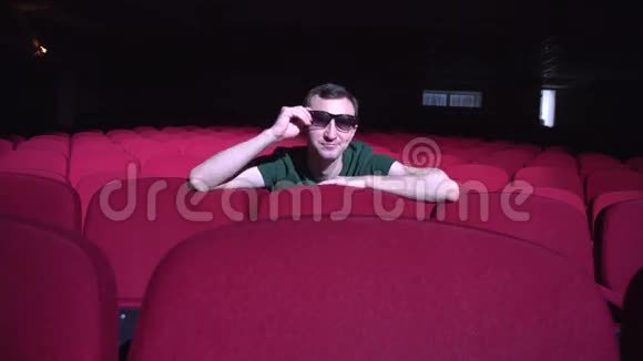 一个男人坐在黑色电影院里舒适的红椅子上看着喜剧和笑声视频的预览图