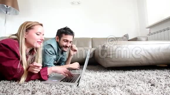 一对可爱的夫妇在家里躺在蓬松的地毯上用笔记本电脑视频的预览图