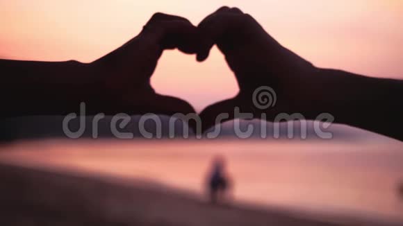 女孩用她的双手在海洋背景上用美丽的金色夕阳做心慢动作1920x1080视频的预览图