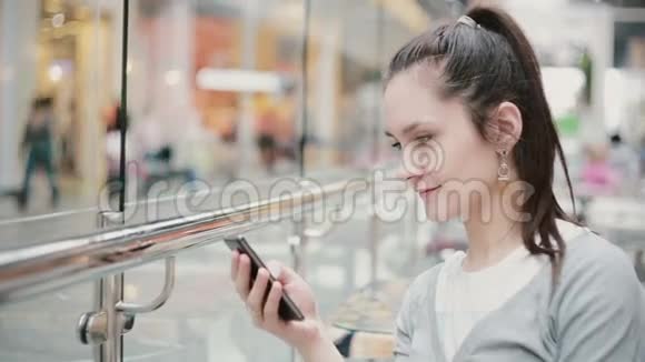 从侧面看一个女孩她坐在公共场所用手机微笑着视频的预览图