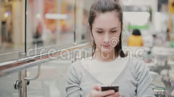 一个穿灰色毛衣的年轻女人用她的智能手机视频的预览图