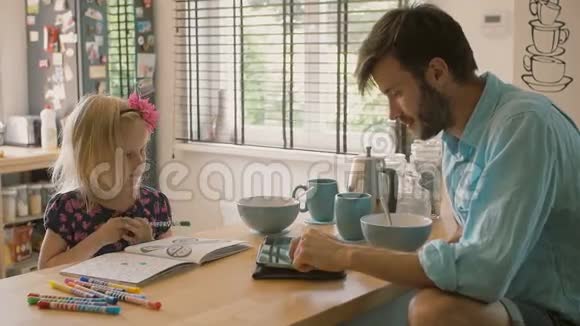 一位父亲正在他的I垫工作而他的女儿正在厨房的桌子上着色慢节奏视频的预览图
