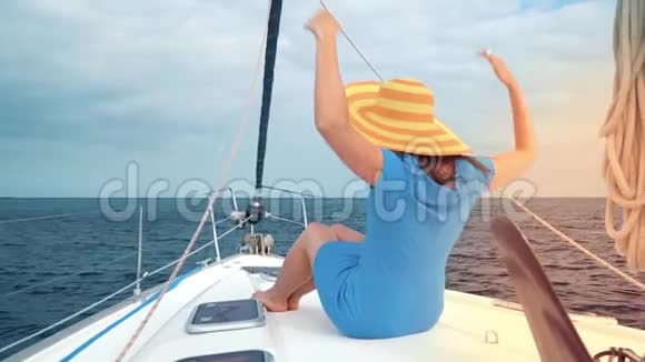 穿着黄色帽子和蓝色裙子的女人在海洋的夏季在游艇上休息慢动作视频的预览图