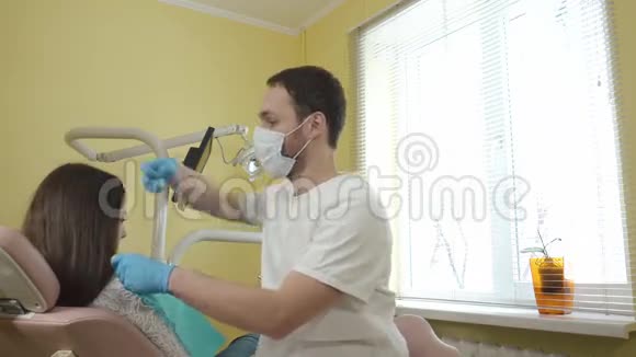 男性牙医准备在牙科诊所检查一名女性病人穿上胸部无菌布视频的预览图