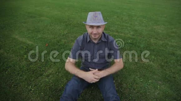 时尚年轻人戴着帽子坐在草地上摆姿势视频的预览图