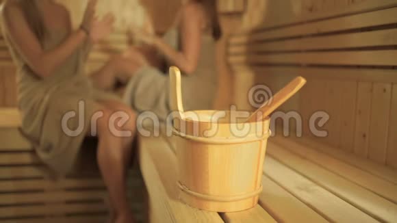 在两个女孩的背景下在桑拿浴室里放有勺子的木桶视频的预览图
