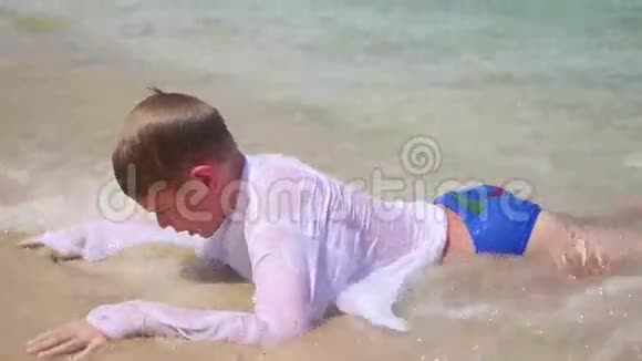 快乐的孩子躺在海滩上在阳光明媚的日子里在海浪中游泳视频的预览图
