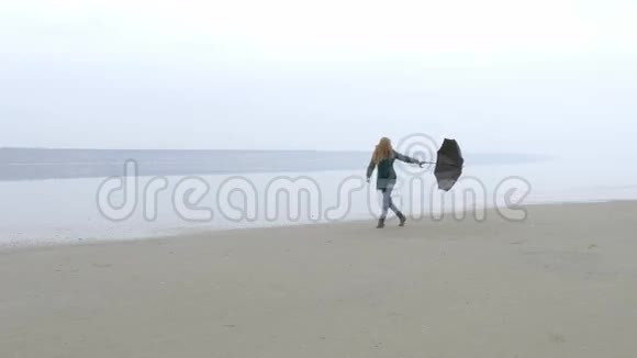 年轻漂亮的女孩从右到左打着伞在沙滩上散步视频的预览图