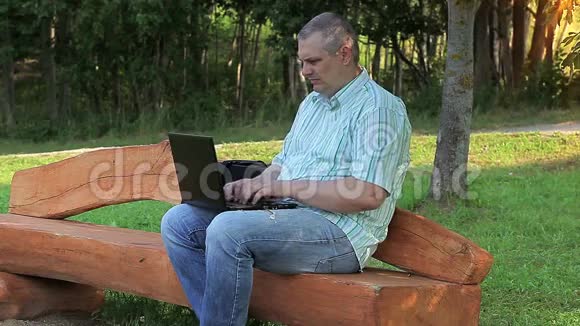 坐在长凳上的公园里拿着笔记本电脑的累人视频的预览图