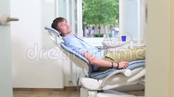 微笑男病人坐在牙科椅上等牙医来视频的预览图