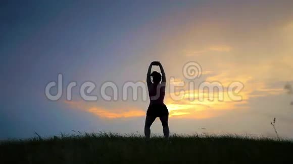 健康的女人在橘红色的阳光下坐摆莲花姿势视频的预览图
