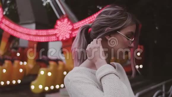 戴眼镜的年轻姑娘在游乐园里抚摸着秋千附近的头发视频的预览图