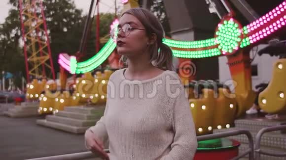 迷人的女孩戴着眼镜在游乐园里抚摸着秋千附近的头发视频的预览图