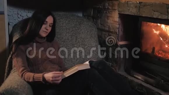 美丽的年轻女子读书书坐在壁炉旁特写镜头假期和生活方式概念视频的预览图