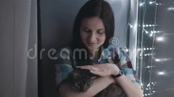 美丽迷人的女人盯着一只猫坐在窗台上装饰着花环视频的预览图