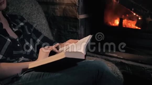 美丽的年轻女子读书书坐在壁炉旁密切关注度假和生活方式的概念视频的预览图