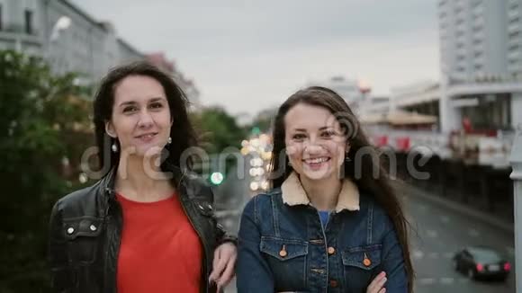 两个美丽的女孩站在桥上微笑着笑着看着镜头风吹着他们的长发视频的预览图