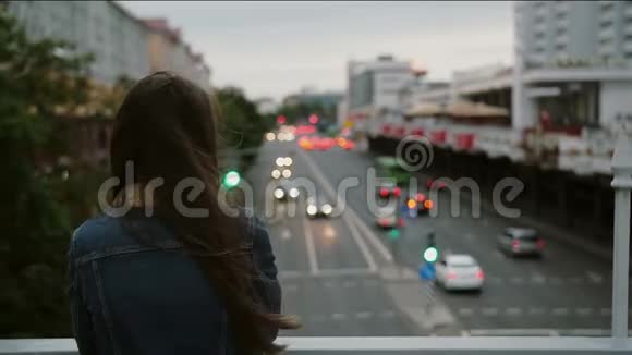 美丽的女孩站在桥上看着城市然后转向相机微笑风吹着她的头发慢节奏视频的预览图