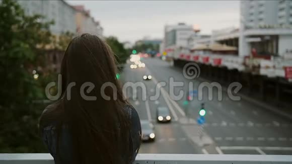 美丽的女孩站在桥上看着城市风吹着她的头发后视慢动作视频的预览图