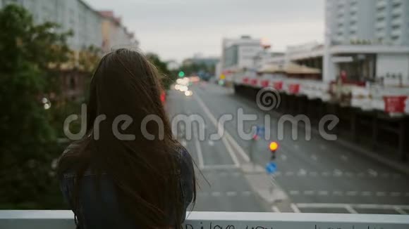美丽的女孩站在桥上看着城市风吹着她的头发后视慢动作视频的预览图